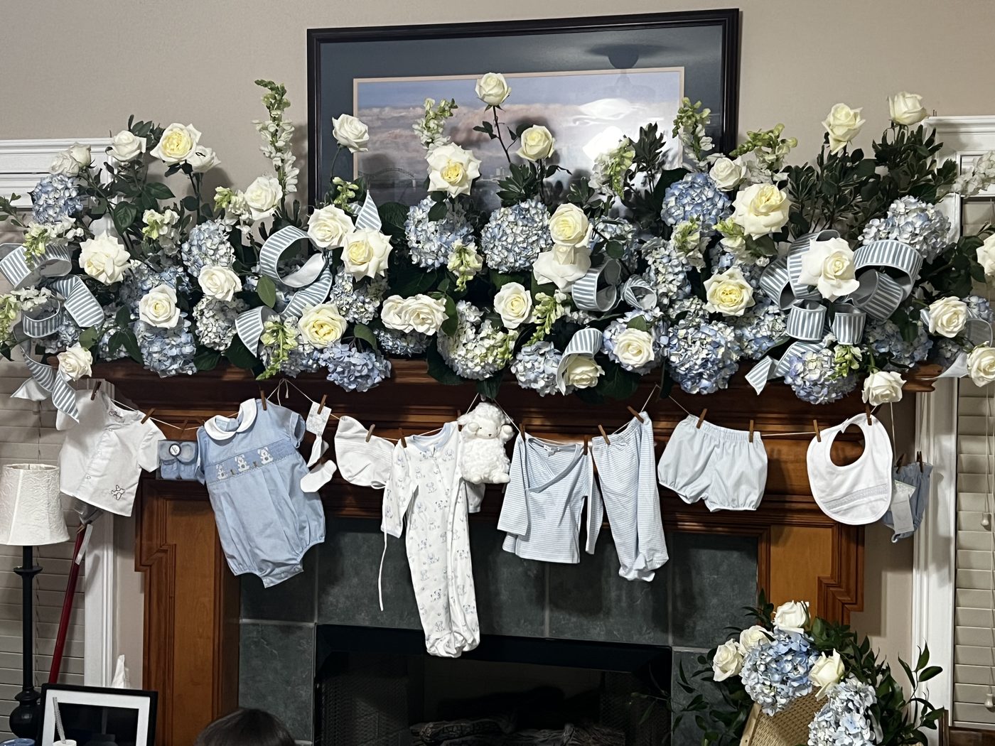 Baby shower mantel with blue hydrangea and hanging baby clothes